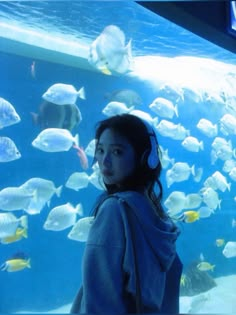 a girl wearing headphones standing in front of a large aquarium filled with lots of fish