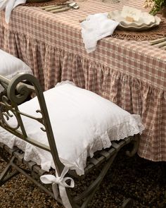 the table is set with two white pillows and place settings on it, along with an old fashioned iron bench