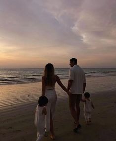 a man and woman holding hands while walking with two children on the beach at sunset