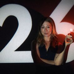 a woman holding a lit candle in front of the number twenty two sign at night