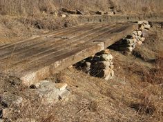 an old wooden bench sitting in the middle of a dry grass covered field with rocks