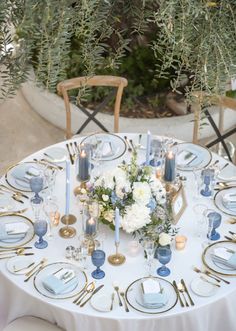 the table is set with blue and white plates, silverware, flowers and candles