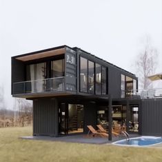 a house made out of shipping containers with a swimming pool in the foreground and deck chairs on the lawn