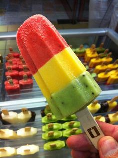 a hand holding an ice cream popsicle with different colored toppings in front of a store display