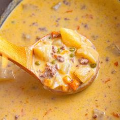 a wooden spoon filled with soup on top of a pan covered in cheese and meat