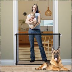 a woman holding a baby standing next to a dog