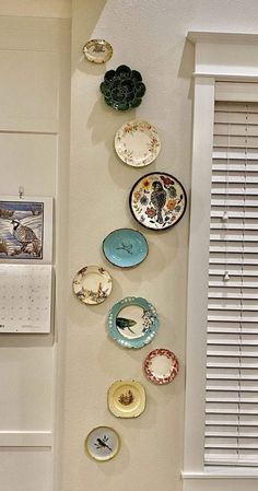 several plates are hanging on the wall next to a calendar and window with shutters