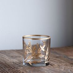 a glass with gold leaves on it sitting on top of a wooden table next to a wall