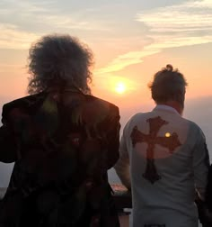 three people standing on top of a hill looking out at the sun in the distance