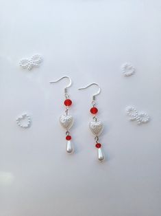 two pairs of heart shaped earrings with red beads hanging from the earwires on a white surface