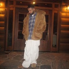 a man standing in front of a door wearing a brown jacket and white pants with his hands in his pockets