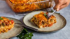 two plates with lasagna casserole on them, one has a fork in it