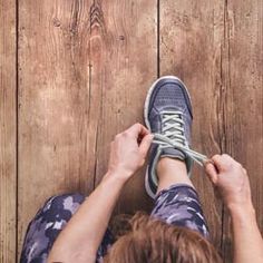 a woman tying up her shoes on the floor with one shoe lace in front of her