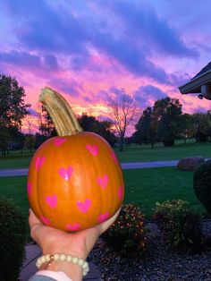 a person holding up a pumpkin with hearts painted on it in front of a sunset