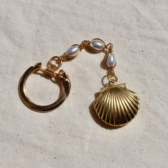 a gold shell charm with pearls hanging from it's side on a white cloth