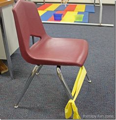 a red school chair sitting in front of a desk with yellow tape on the legs