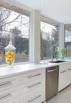 a kitchen with white cabinets and stainless steel dishwasher in front of large windows