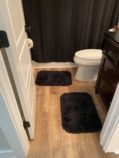 two black rugs on the floor in a bathroom next to a toilet and sink