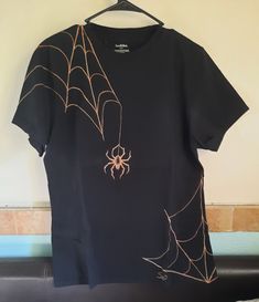 a black t - shirt with a spider on it hanging from a hanger in front of a wall