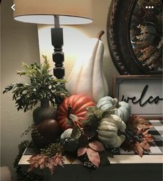 an arrangement of pumpkins, gourds and leaves on a table with a lamp