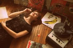 a woman laying on the floor next to an old record player and other records with her eyes closed