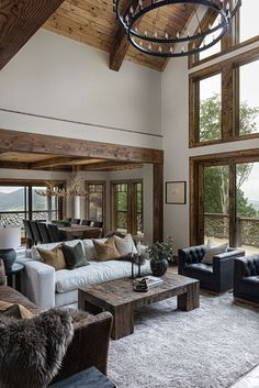 a living room filled with lots of furniture next to large windows and a chandelier hanging from the ceiling