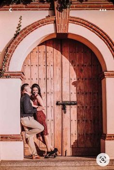 a man and woman standing in front of a wooden door with archs on either side