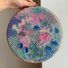 a hand is holding an embroidery project with blue beads and pink flowers