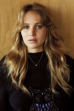 a woman with long blonde hair wearing a black sweater and flowered necklace is looking at the camera