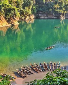 several canoes are lined up on the shore of a lake with green water and cliffs in the background