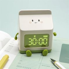 an alarm clock sitting on top of a desk next to a pen and pencils