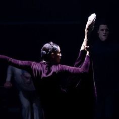 a woman is dancing in the dark with her arms up and hands behind her head