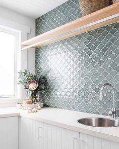 a kitchen with white cabinets and green tiles on the wall, along with a stainless steel sink