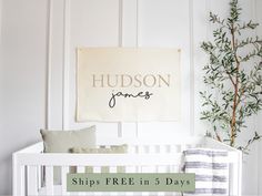 a white crib with a sign that says hudson jones on it and a tree in the corner