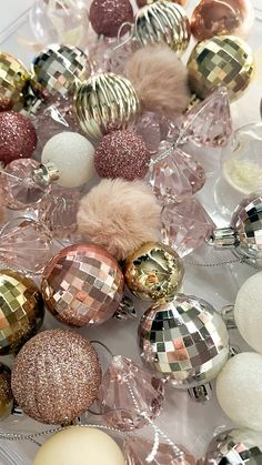 many different colored and shiny ornaments are on the table with white, gold, and silver balls