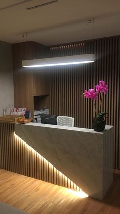 a reception counter with flowers on it in front of a wooden wall and light coming from the ceiling