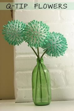 three flowers in a green vase sitting on a white counter top next to a brick wall