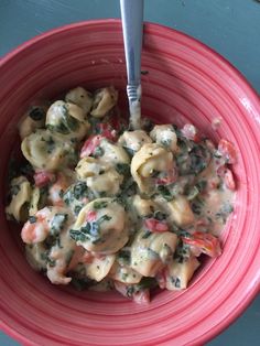 a red bowl filled with pasta and spinach covered in sauce on top of a table