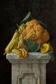 a large head of cauliflower sitting on top of a white vase filled with yellow flowers