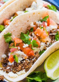 three tacos on a plate with lime wedges