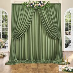 a room with green curtains and flowers on the window sill, surrounded by candles