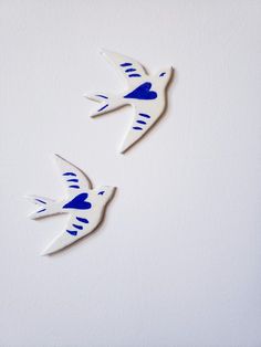 two blue and white birds flying next to each other in the air on a white wall