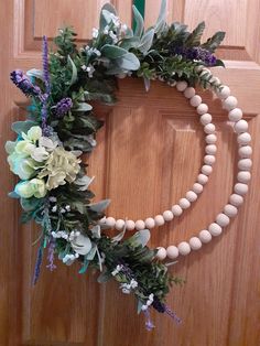 a wooden beaded wreath with flowers and greenery hanging on the front door frame