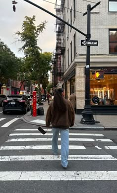 a man walking across a cross walk in front of a tall building with shops on it