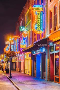 an image of a city street at night with neon signs on the buildings and people walking down the sidewalk