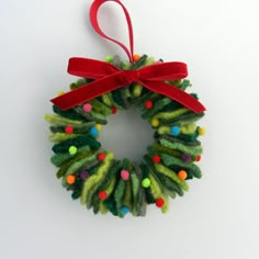 a christmas wreath ornament hanging from a red ribbon on a white background with colorful balls