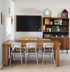 a dining room table with chairs and a chalkboard on the wall