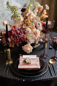 the table is set with black plates and pink napkins, gold place settings and floral centerpieces