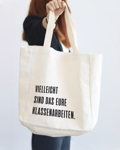 a woman holding a white bag with black writing on the front and bottom, which reads velleightt sind das euroe klassnabbetten