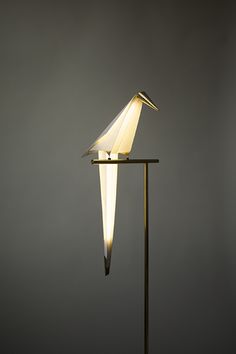 a white bird sitting on top of a metal pole next to a light that is turned on